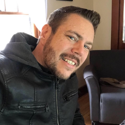 This is a profile image of Michael Daniels. Smiling at the camera with a black jacket on.